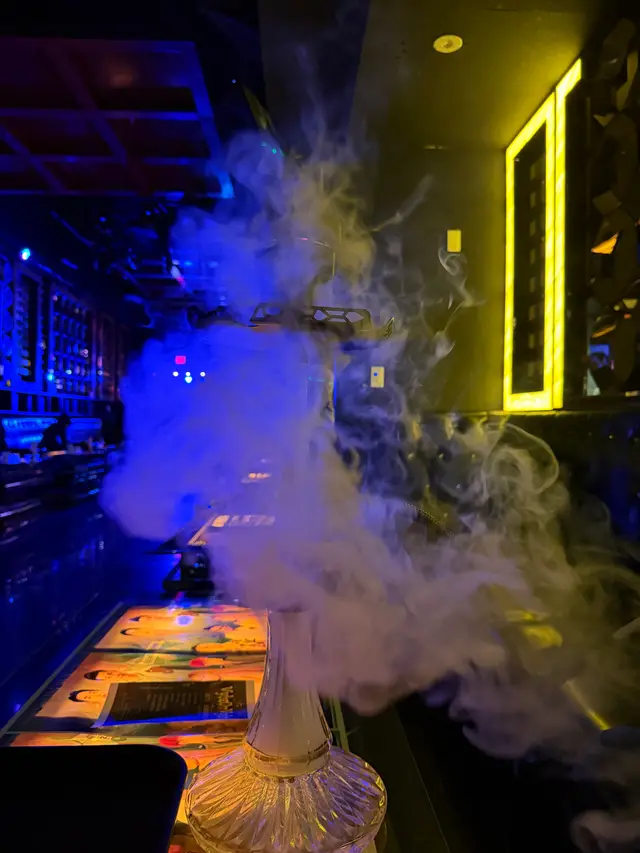 Hookah running on a lounge bar under coloured neon, a thick plume across the room