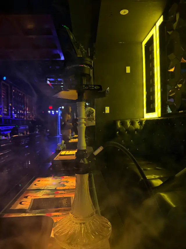 Hookah running on a lounge bar under coloured neon, a thick plume across the room