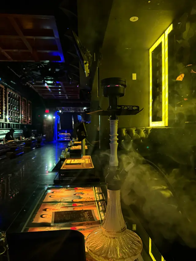 Hookah running on a lounge bar under coloured neon, a thick plume across the room