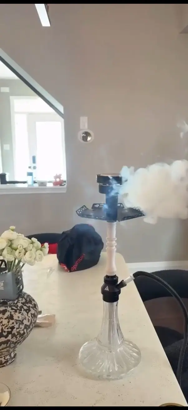 Hookah alight on a table in a bright room, a plume of smoke beside it