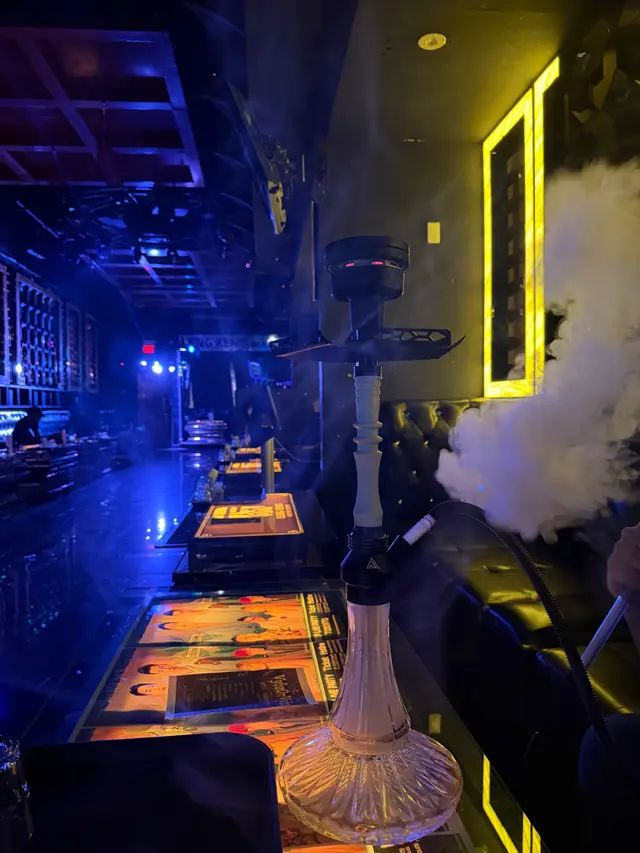 Hookah running on a lounge bar under coloured neon, a thick plume across the room