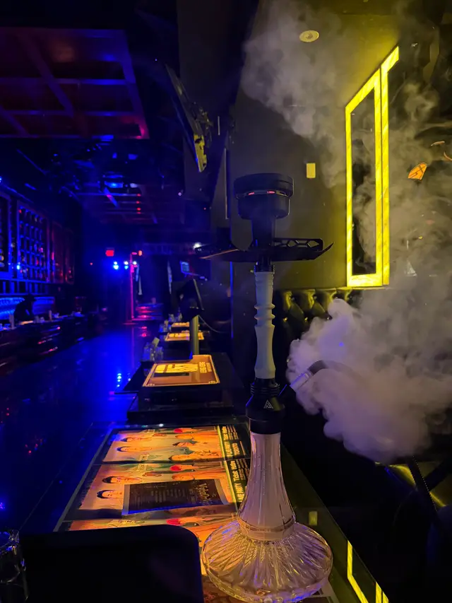 Hookah running on a lounge bar under coloured neon, a thick plume across the room