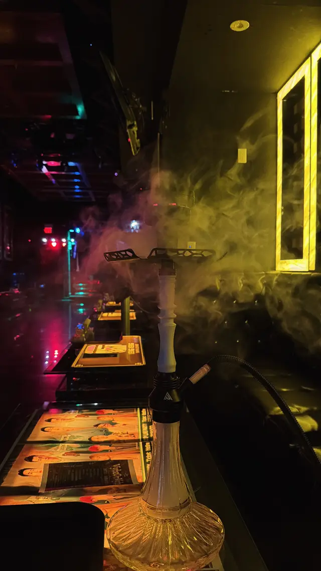 Hookah running on a lounge bar under coloured neon, a thick plume across the room