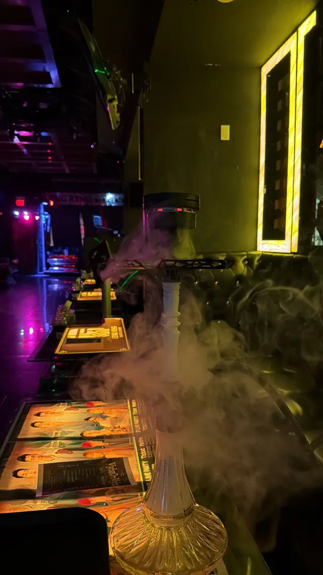 Hookah running on a lounge bar under coloured neon, a thick plume across the room