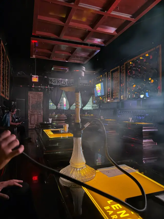 Guest at a hookah on a lounge table, smoke across the bar