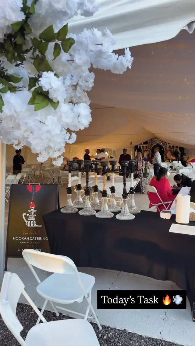 Hookahs laid out on a long table at a marquee event, floral arch behind